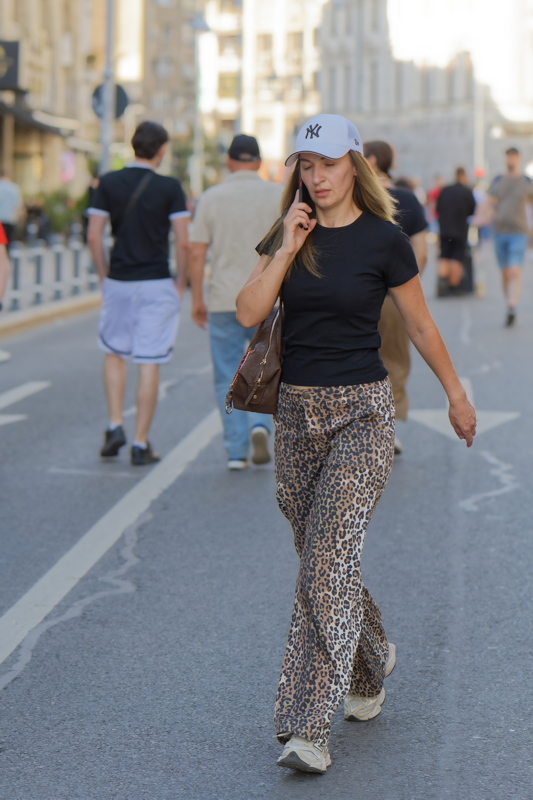 Woman wearing a pair of brown leopard print trousers talking on the phone while walking